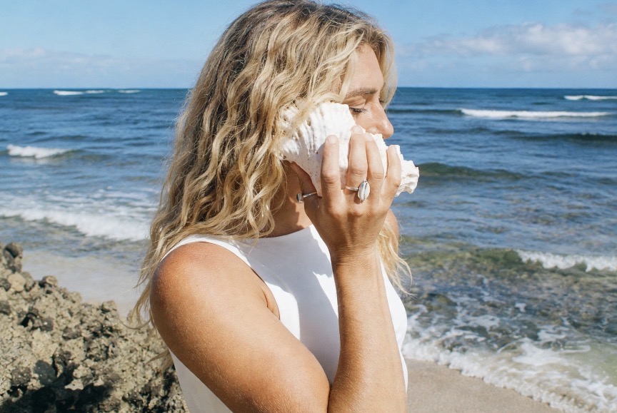Brittany holding a conch shell to her ear by the ocean